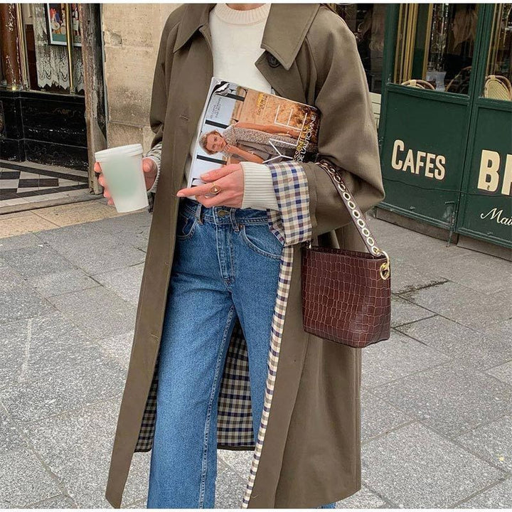 Oversized khaki trench coat worn open over cream sweater and blue jeans