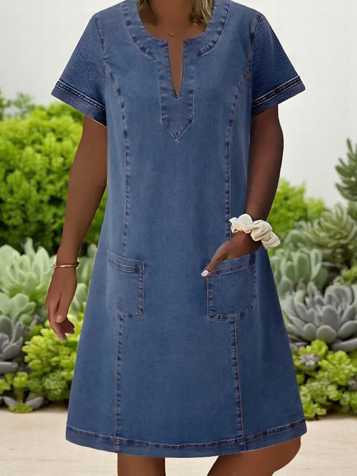 Blue denim shift dress with notched neckline and short sleeves, worn outdoors