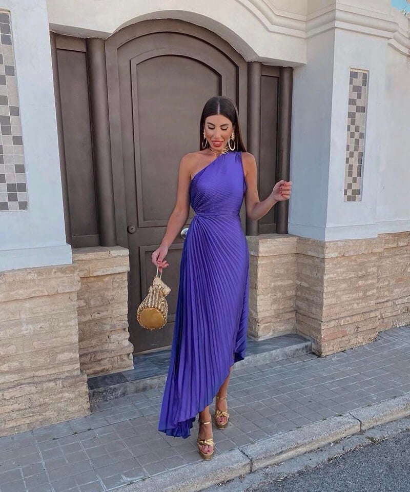 One-shoulder purple pleated midi dress paired with gold platform sandals and mini bag