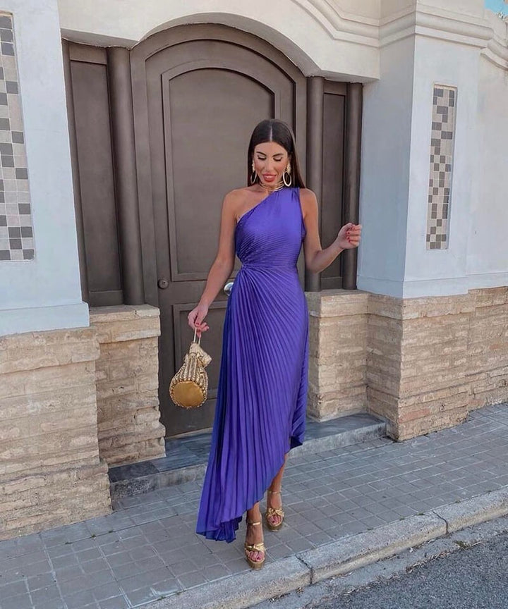One-shoulder purple pleated midi dress paired with gold platform sandals and mini bag