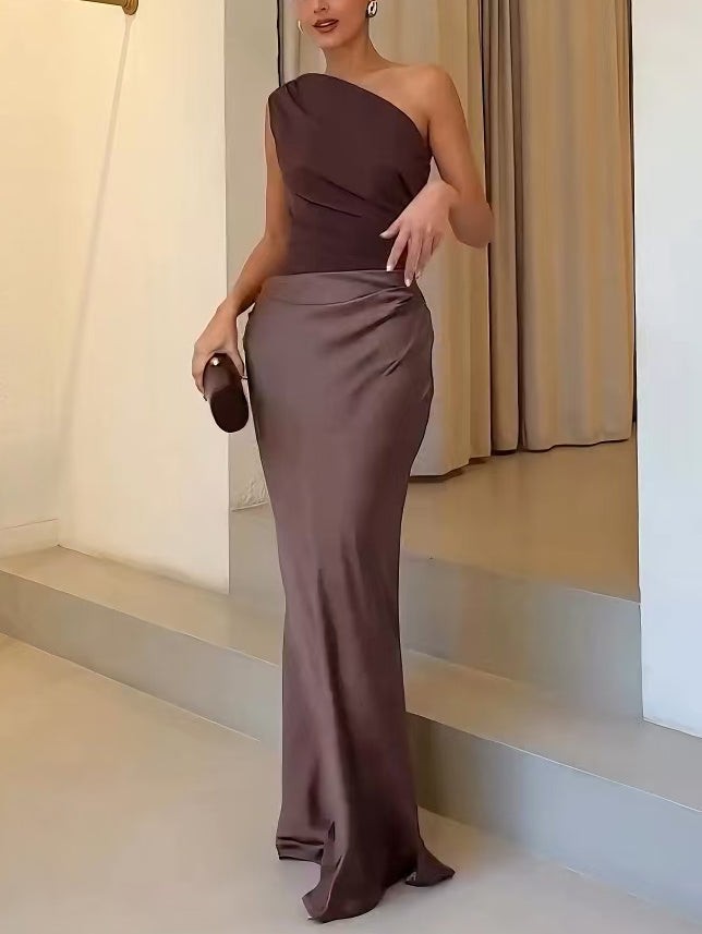 Model holding clutch in one-shoulder brown satin gown with draped skirt