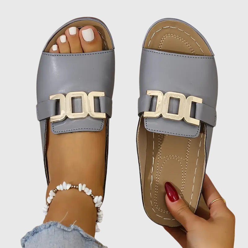 Gray flat slide sandals featuring gold buckle and open toe design