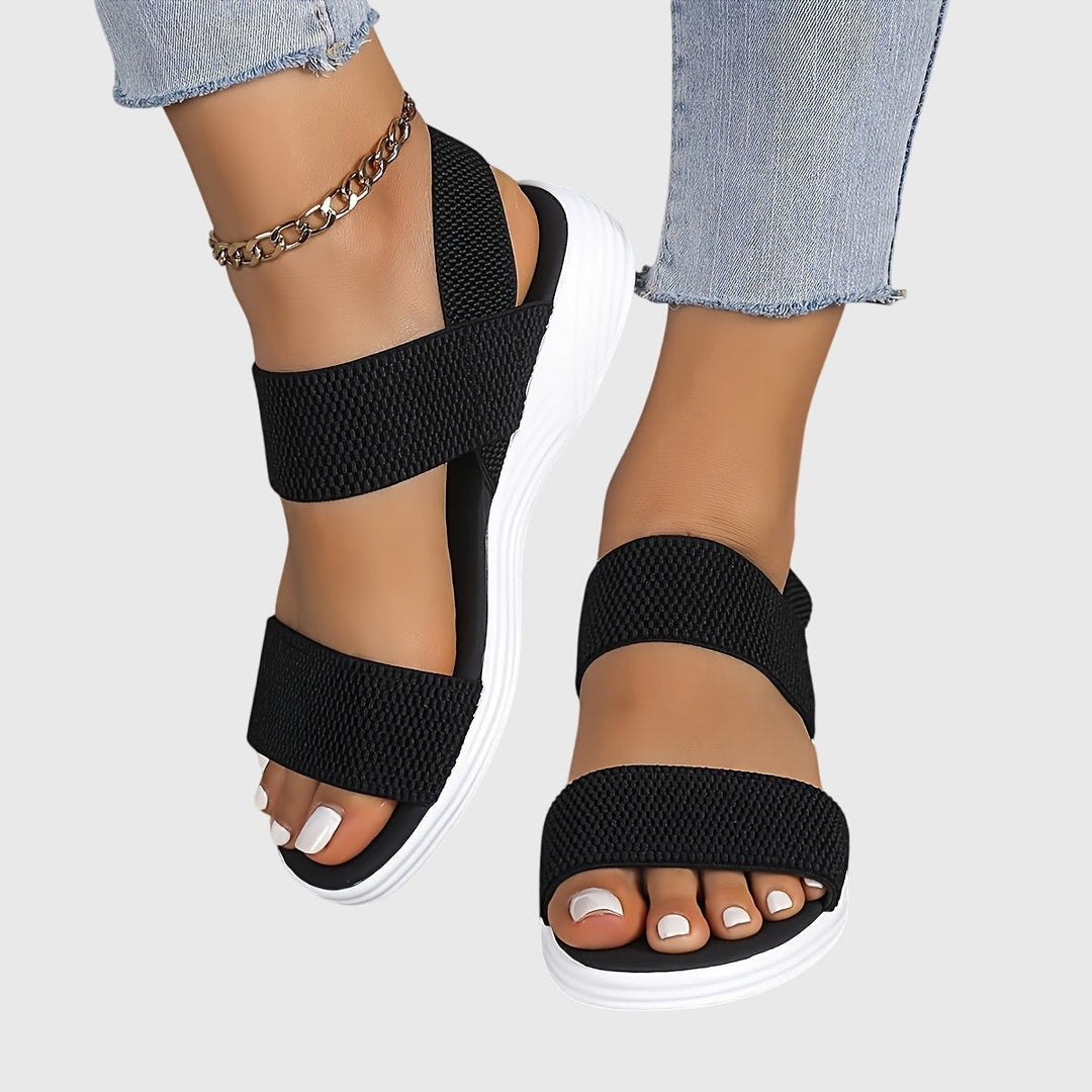 Black woven strap platform sandals with white sole and ankle chain accent