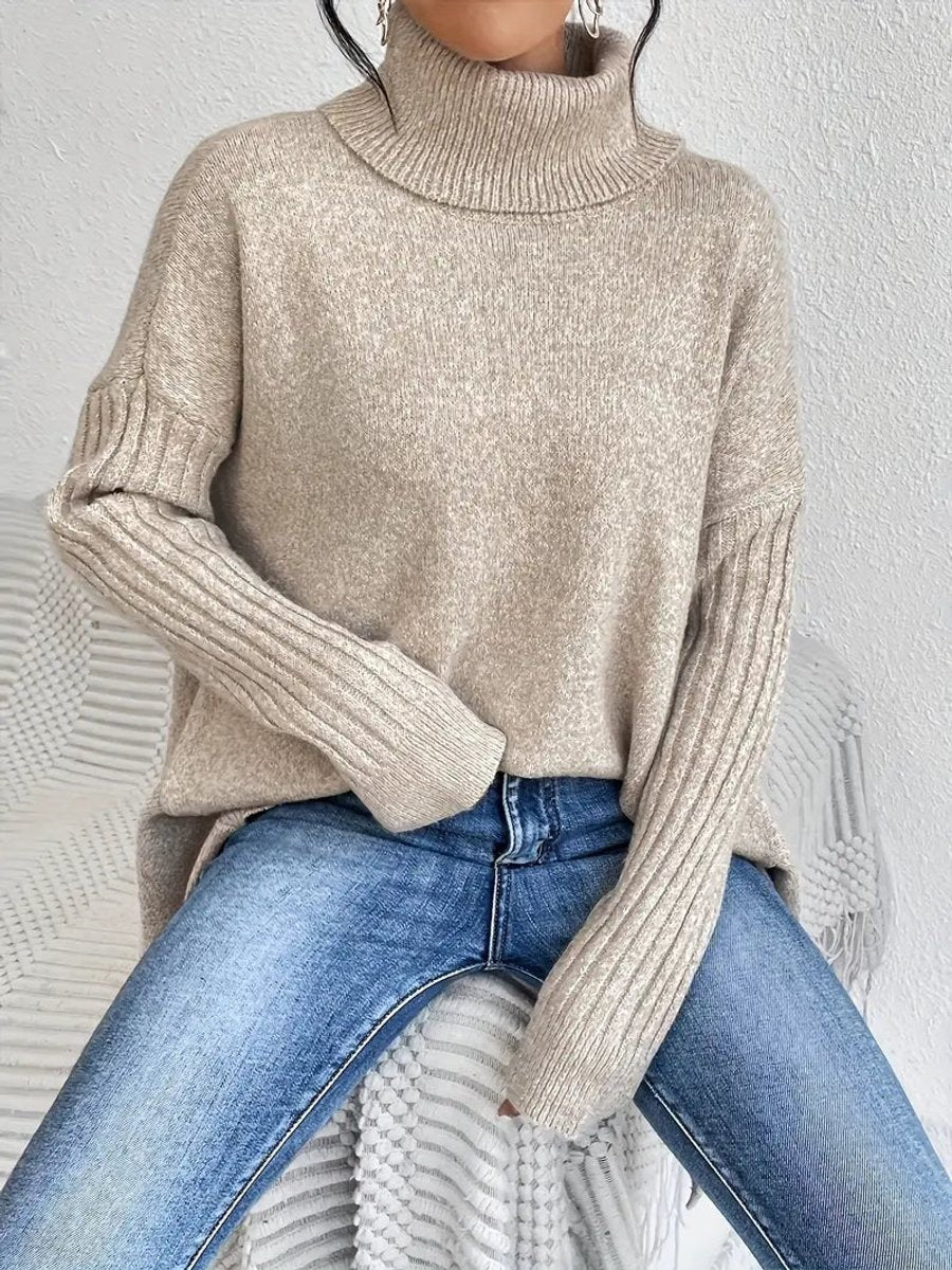 Seated model wearing beige ribbed-trim turtleneck sweater with jeans, close-up view