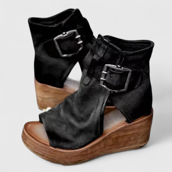 Black suede peep-toe wedge booties featuring silver buckle detail and stacked heel