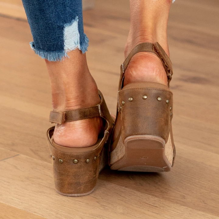 Back view of brown suede wedge sandals highlighting studded heel and ankle strap