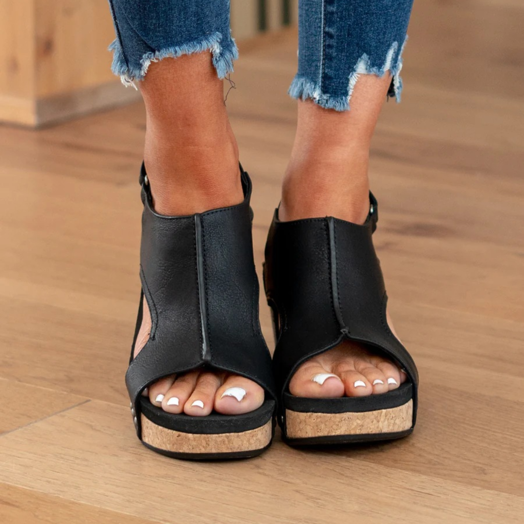 Black faux leather peep-toe wedge sandals with cork platform, worn with jeans
