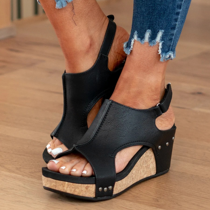 Black wedge sandals showing cutout ankle straps and studded cork heel