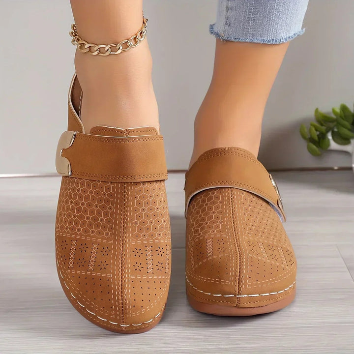 tan perforated wedge clog featuring embossed pattern and gold accent