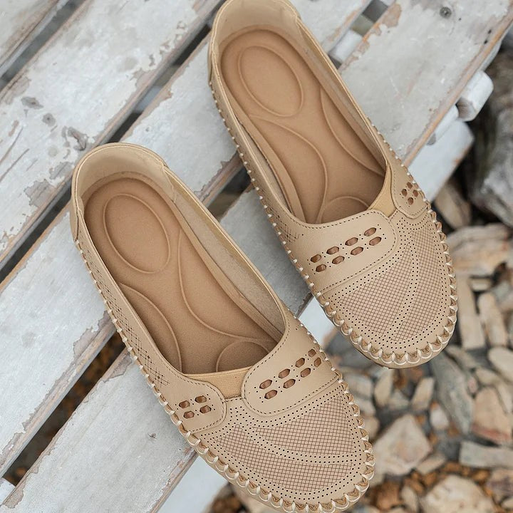 beige perforated flats with contrast stitching displayed on wooden slats