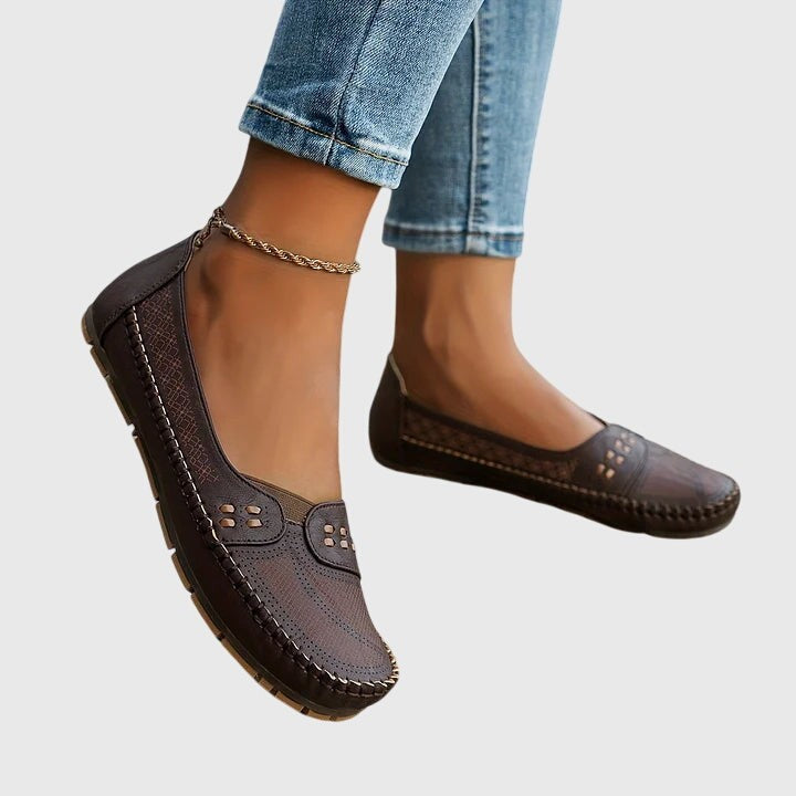 Dark brown leather flats with perforated pattern, worn on feet