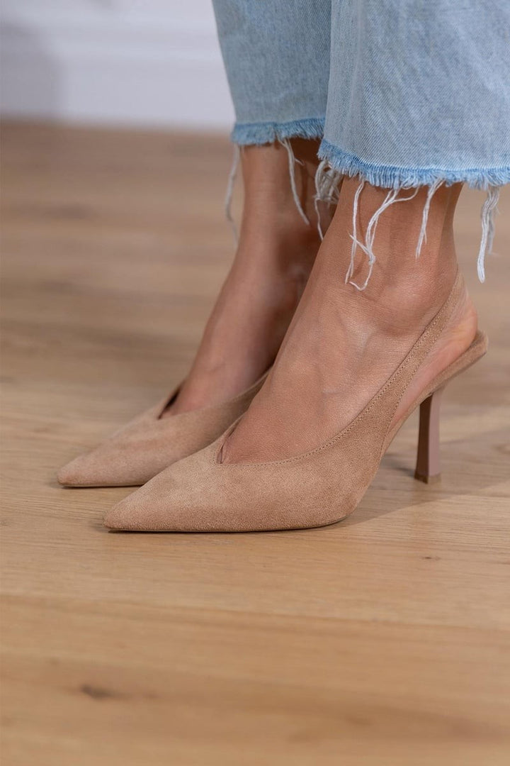 Pointed toe tan suede pumps with slingback strap on wood floor