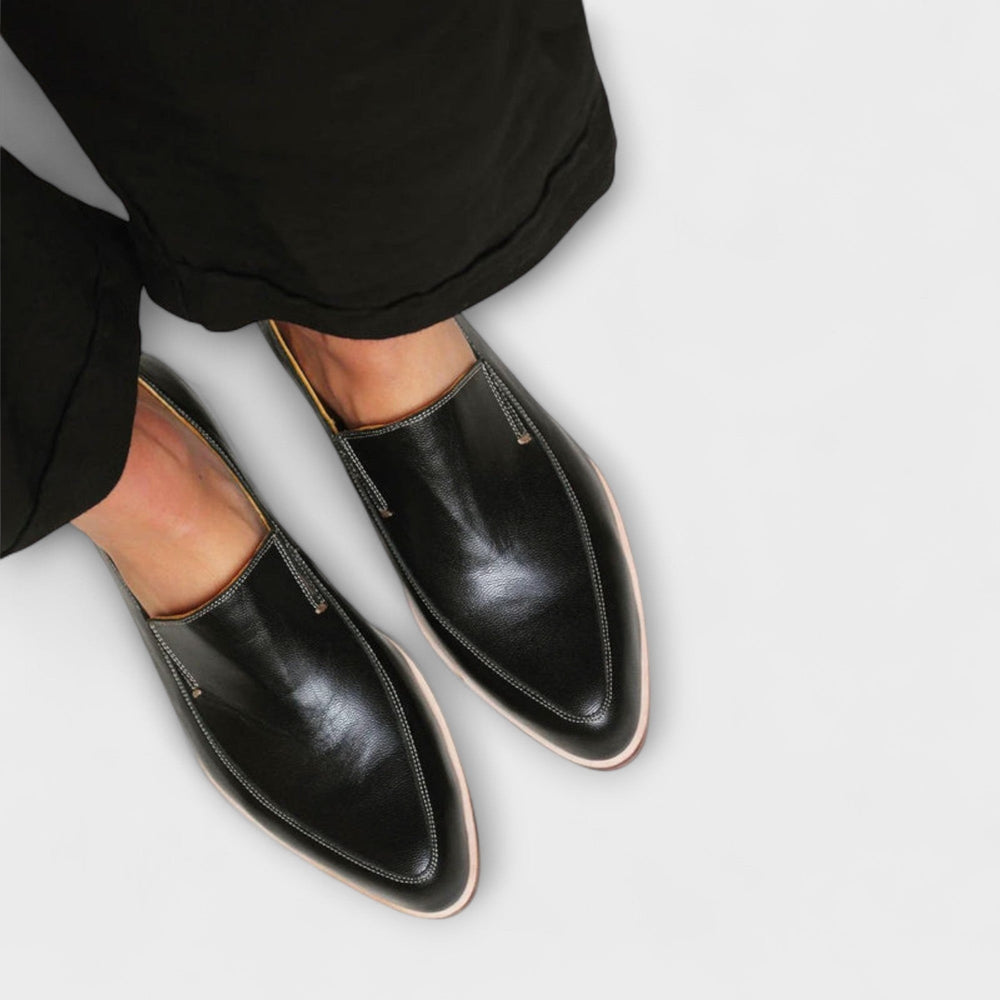 Close-up of black leather slip-on loafers featuring pointed toe and beige piping