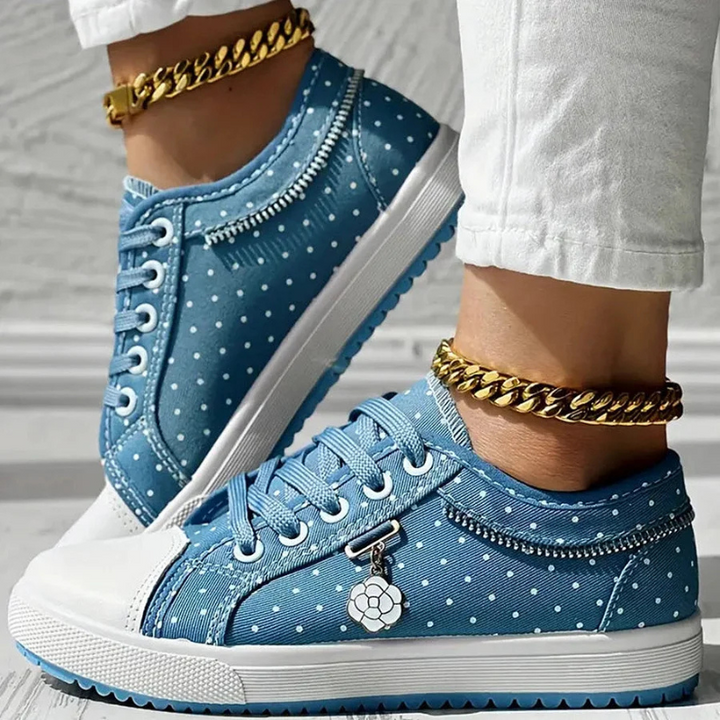 Navy and white polka dot sneakers hanging against a textured white wall