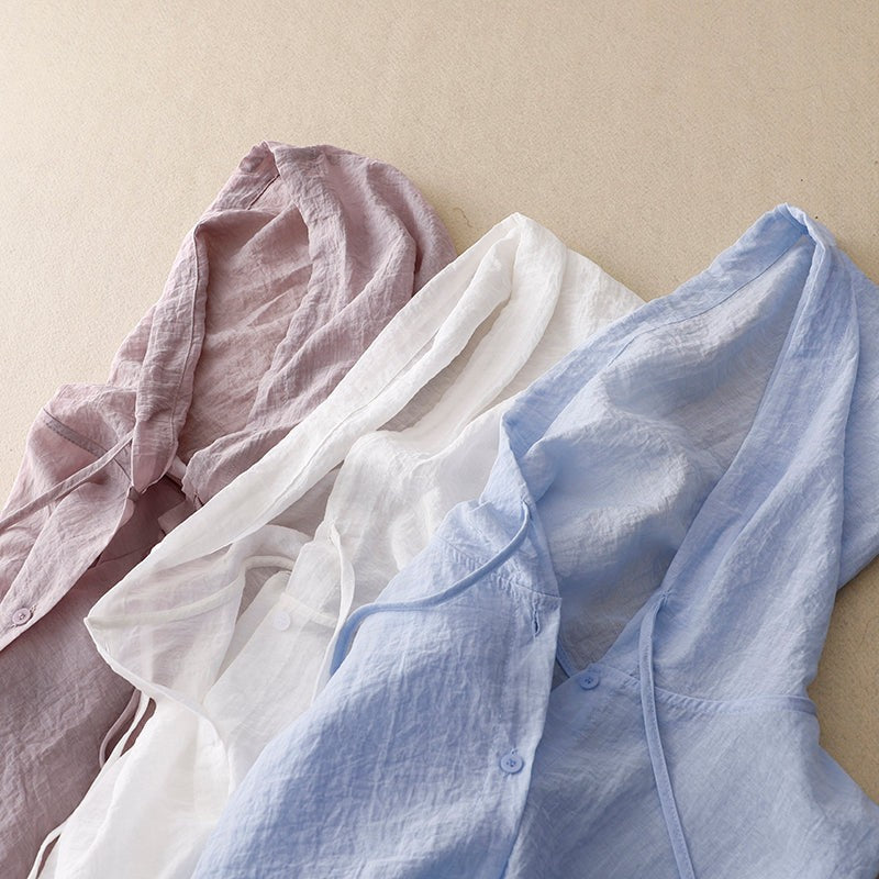 Pink, white, and blue linen hooded shirts folded together showing color options