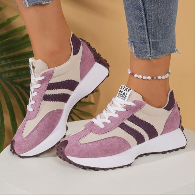 Pink and beige retro sneakers with purple stripes displayed on white pedestal