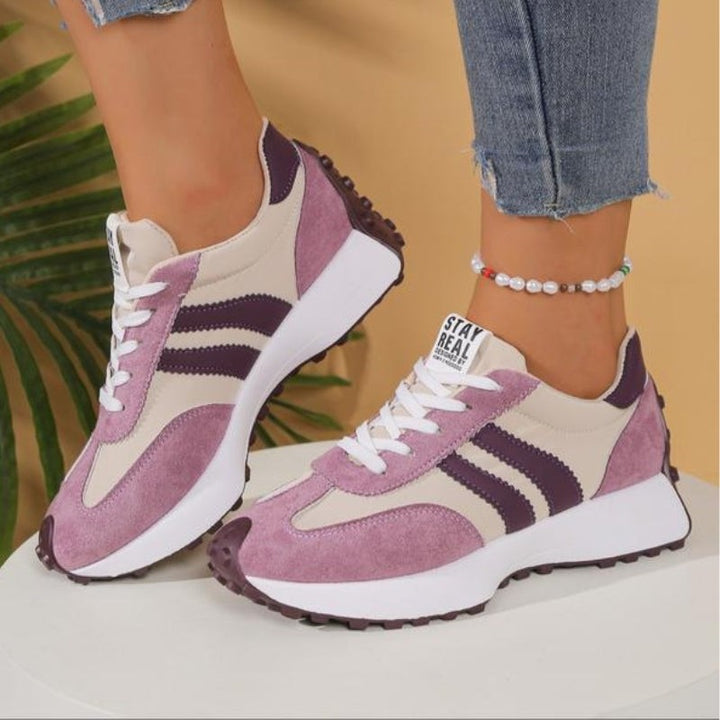 Pink and beige retro sneakers with purple stripes displayed on white pedestal