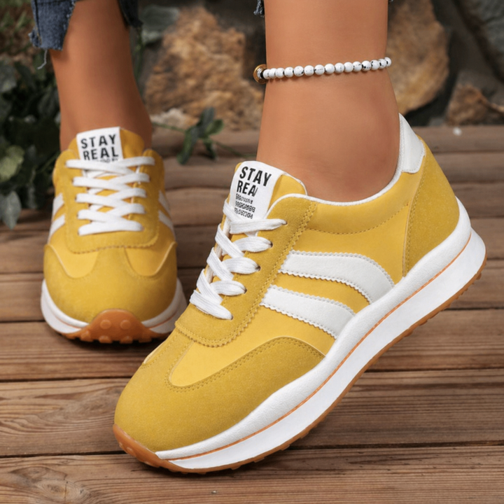 Mustard yellow suede platform sneakers with white stripe detailing on wood deck