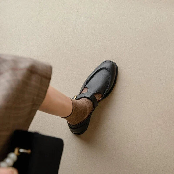 Black leather Mary Jane shoe with stitched apron toe against a beige wall