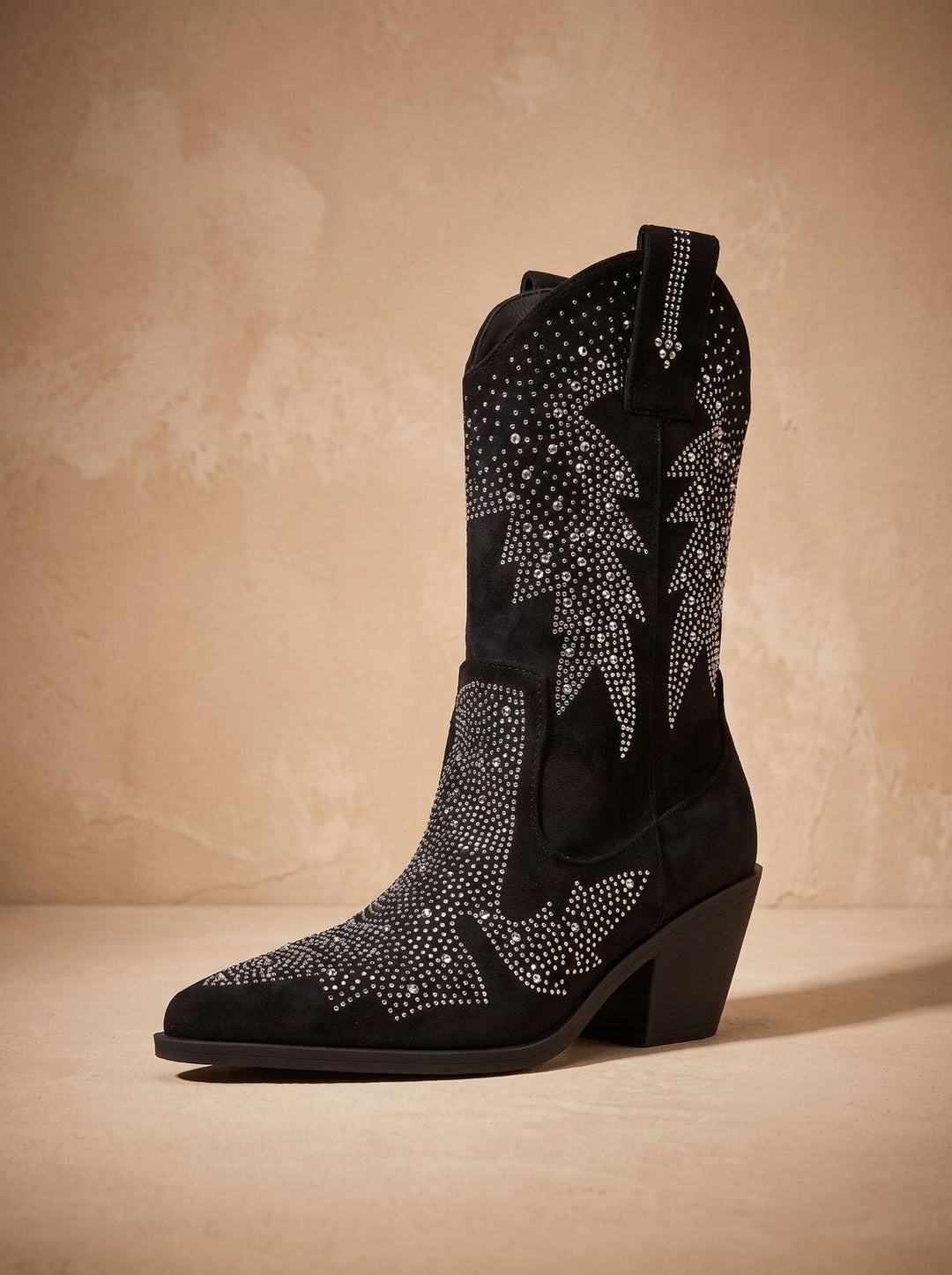 Single black western boot displaying rhinestone detailing against textured beige backdrop