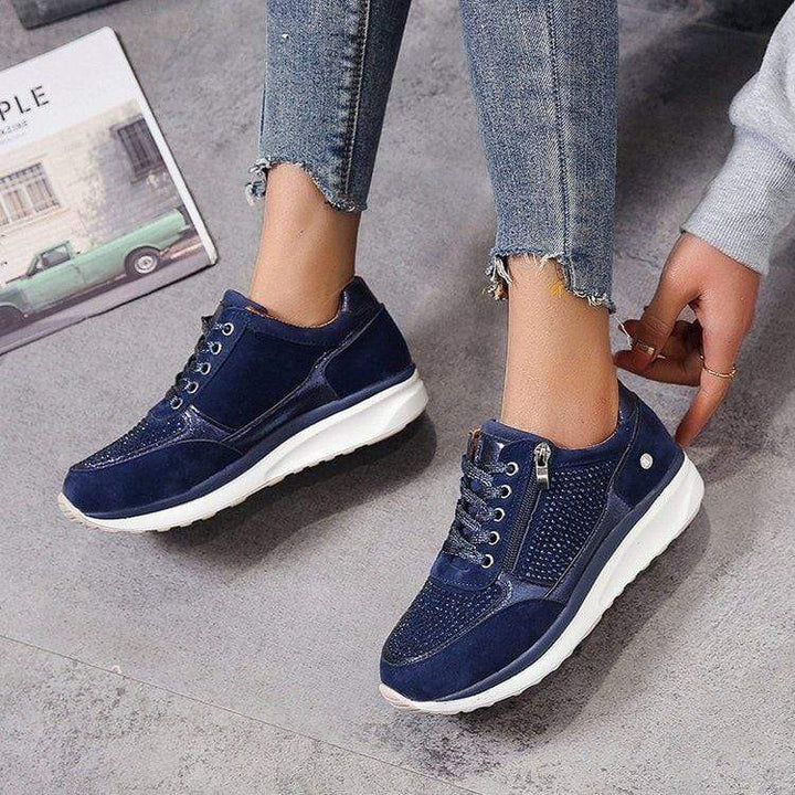 Navy blue platform sneakers with rhinestone detailing and side zipper, worn with jeans