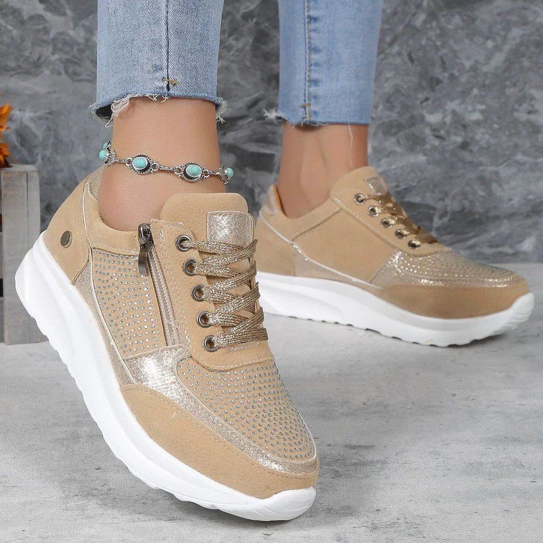 Beige platform sneakers with gold metallic trim and rhinestone mesh detailing worn on foot