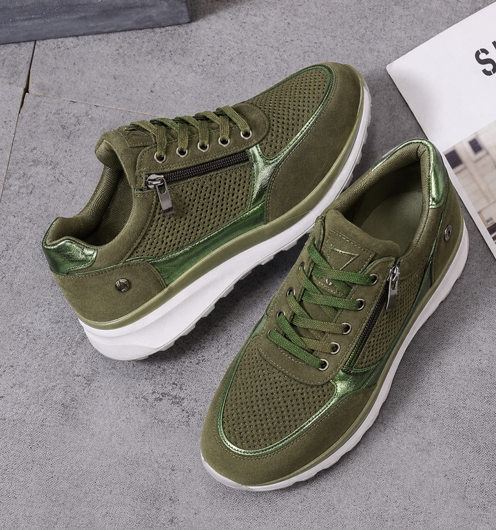 Pair of olive green platform sneakers with zipper and metallic trim resting on floor
