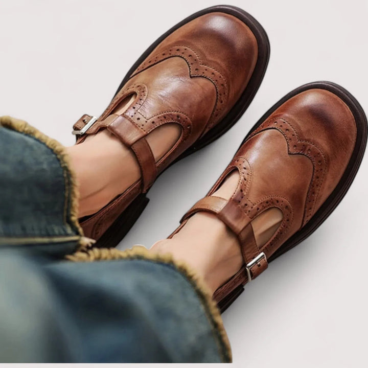 Brown leather Mary Jane shoes with wingtip brogue detailing and buckle strap, worn on feet