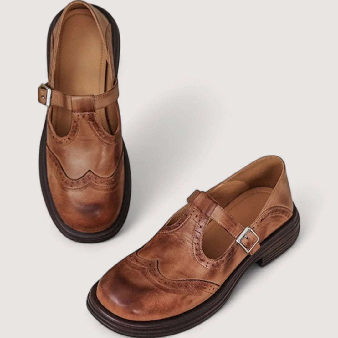 Brown leather Mary Jane shoes with brogue wingtip stitching and adjustable buckle strap