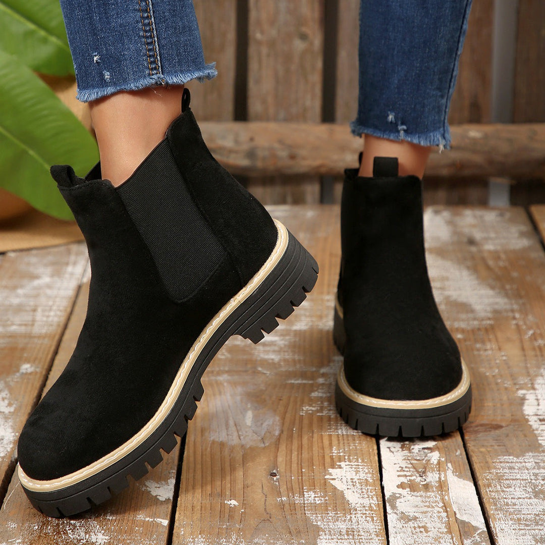 Black suede Chelsea boots with elastic panel viewed from behind on wood