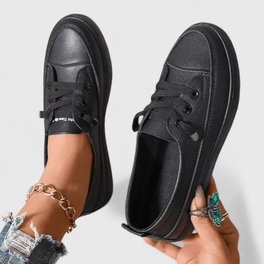 Black leather platform sneakers held in hand showing lace-up design