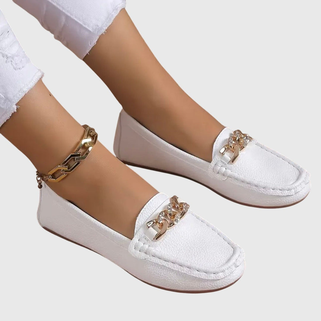 White slip-on loafers with sparkling chain detail, worn with white jeans