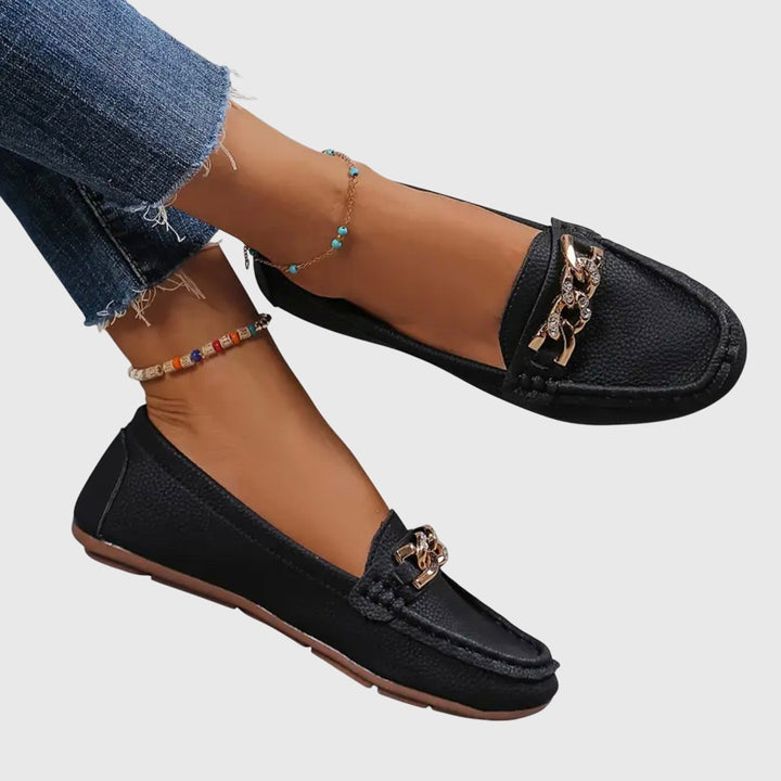 Black leather slip-on loafers featuring gold chain and rhinestone accent