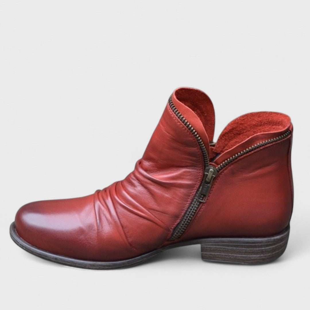 Red leather ankle boot showing draped folds and asymmetric zip trim