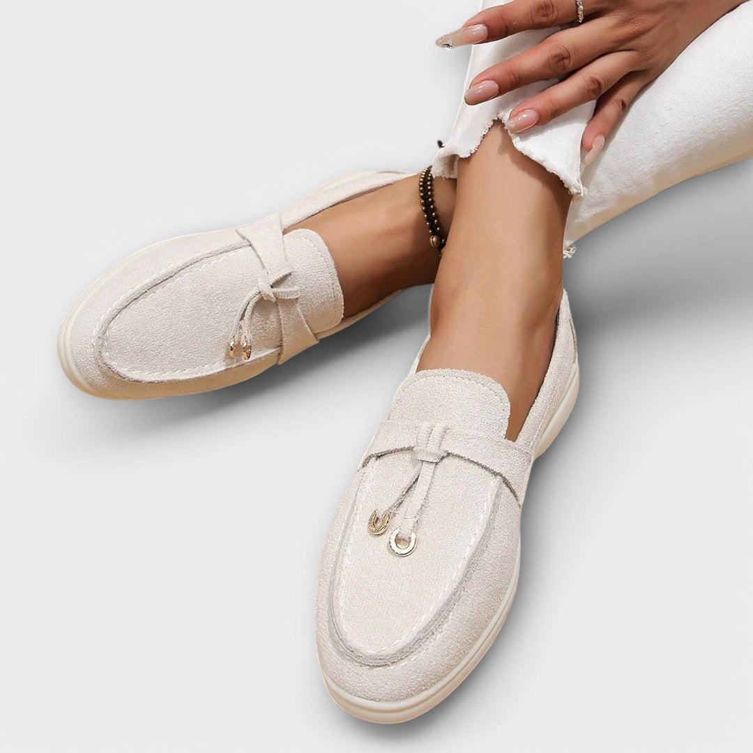 Cream suede loafers featuring gold tassel hardware and flat sole
