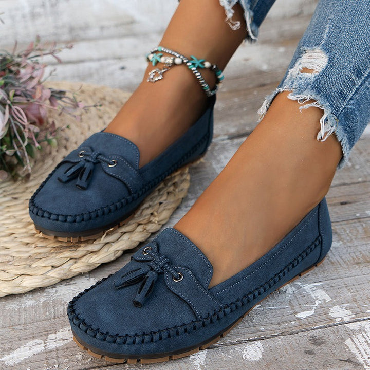 Navy blue suede tassel loafers with whipstitch trim worn on bare feet