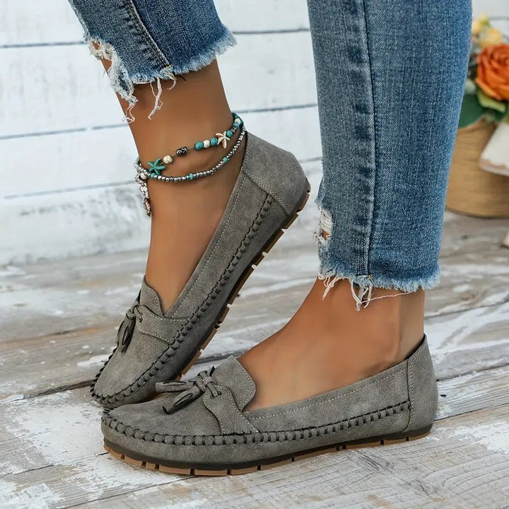 Gray suede tassel loafers worn outdoors with ripped denim jeans