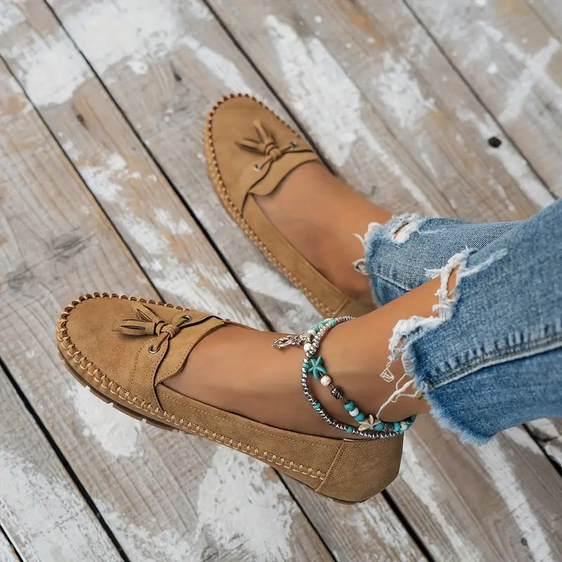 Camel suede loafers with tassel bow shown resting on model's foot