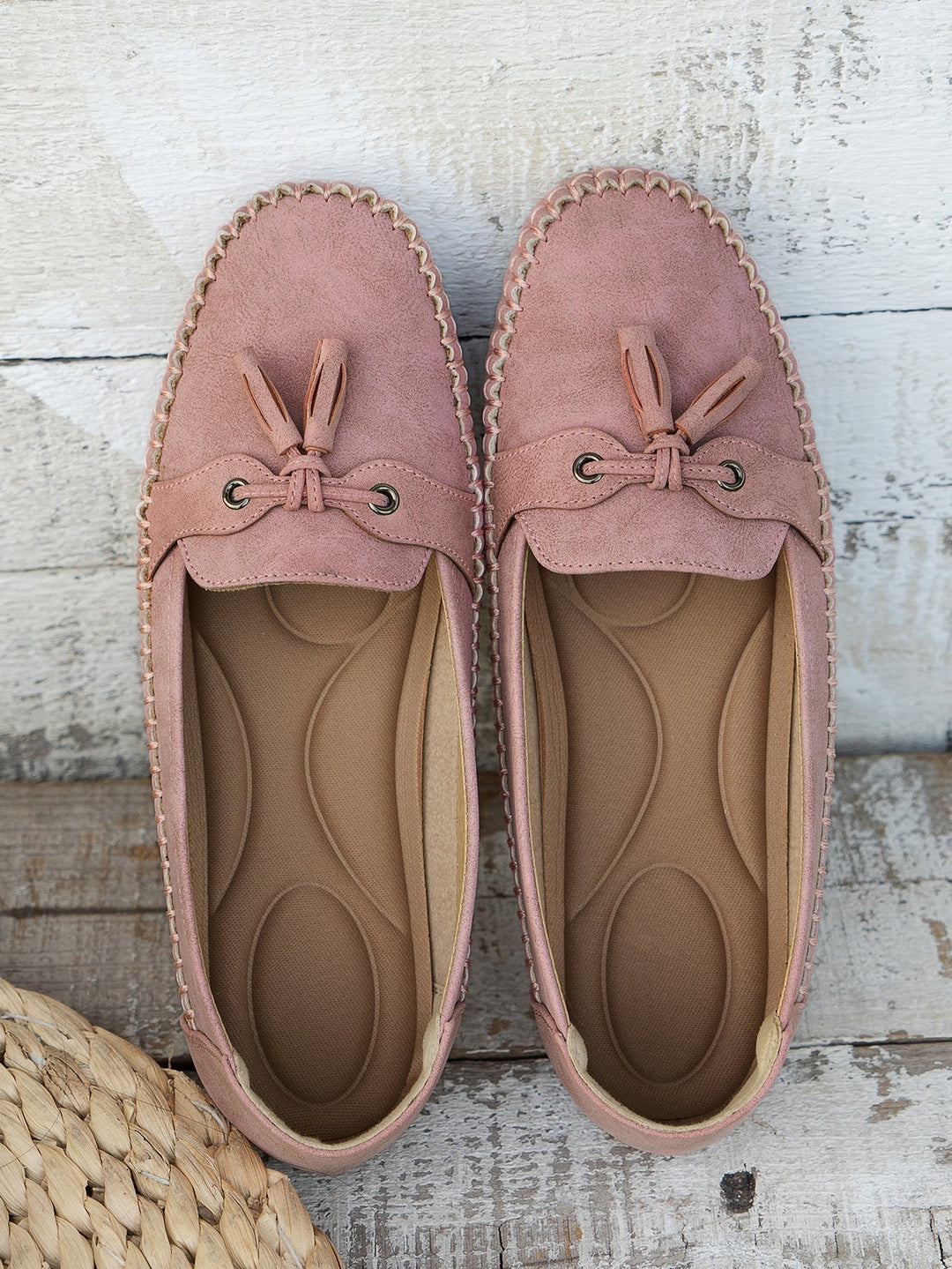 Dusty pink suede loafers with tassel bow displayed top-down on wood floor