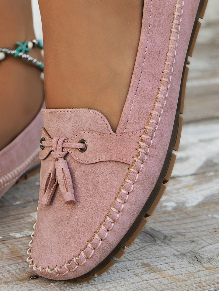 Close-up of pink suede loafer heel with tassel bow and stitched trim