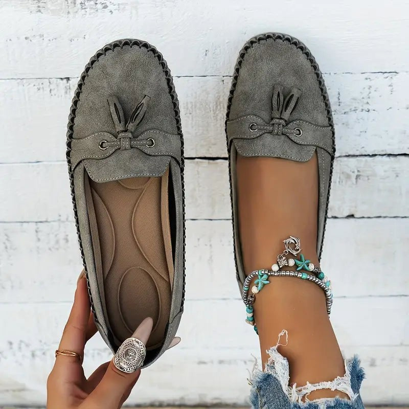 Gray suede tassel loafers displayed side by side against wood backdrop