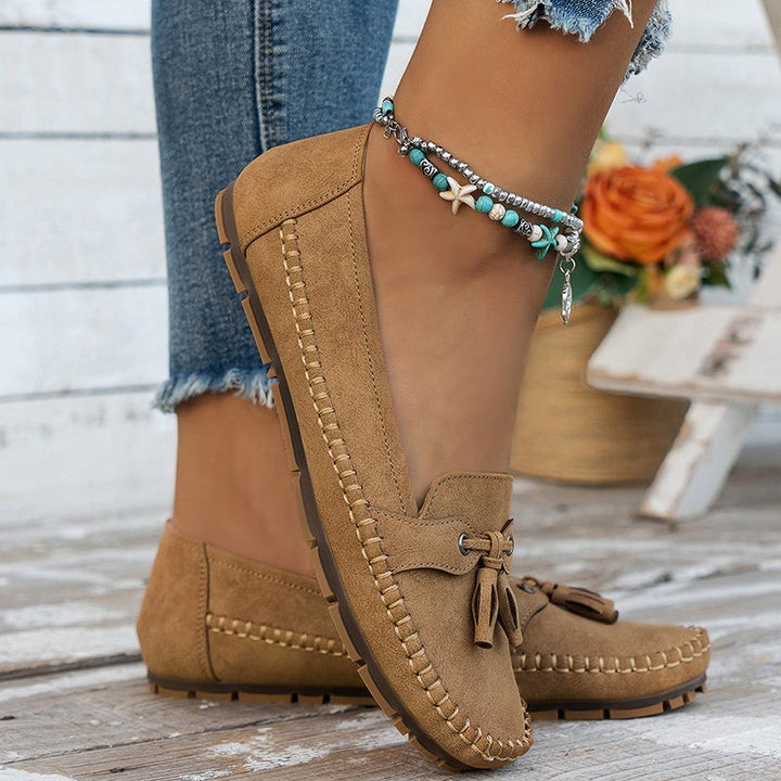 Tan suede moccasin loafers with whipstitched trim on rustic wood floor