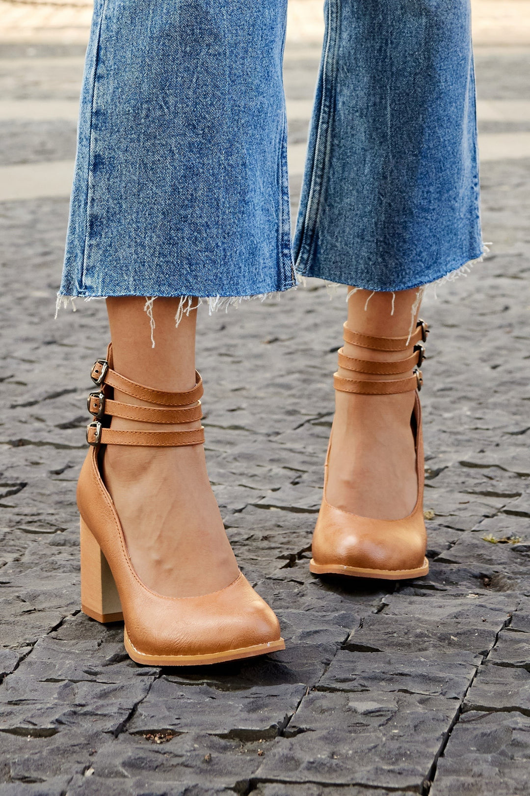 Camel leather block-heel pumps with buckled ankle straps, back view on cobblestone