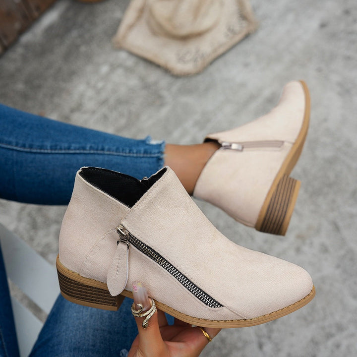 Beige suede ankle boots with side zip and block heel, held by hand