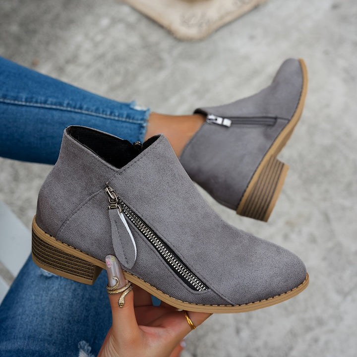 Grey suede ankle boots with silver zip pull held in hand
