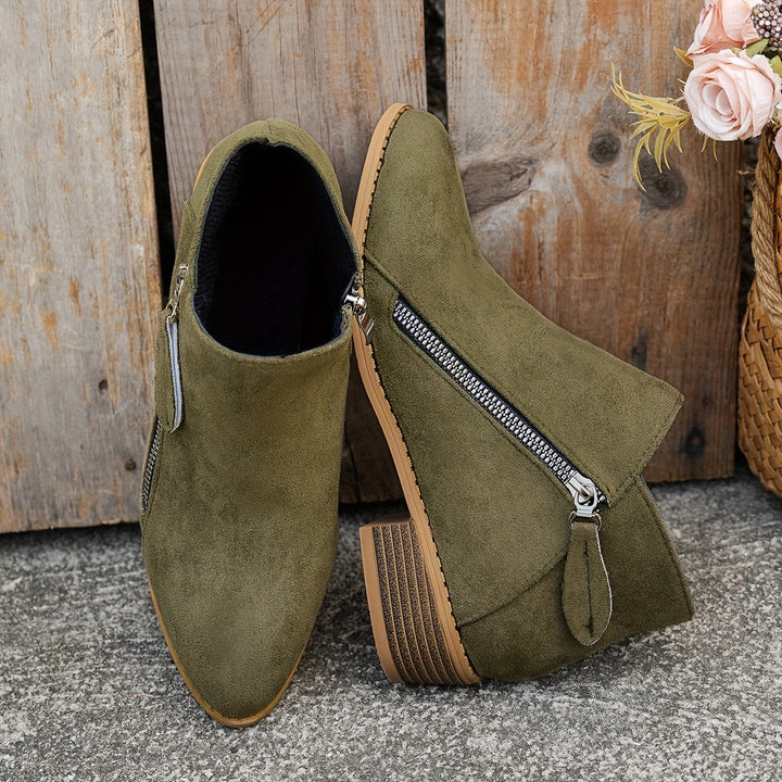 Olive green suede ankle boots paired together against wooden backdrop