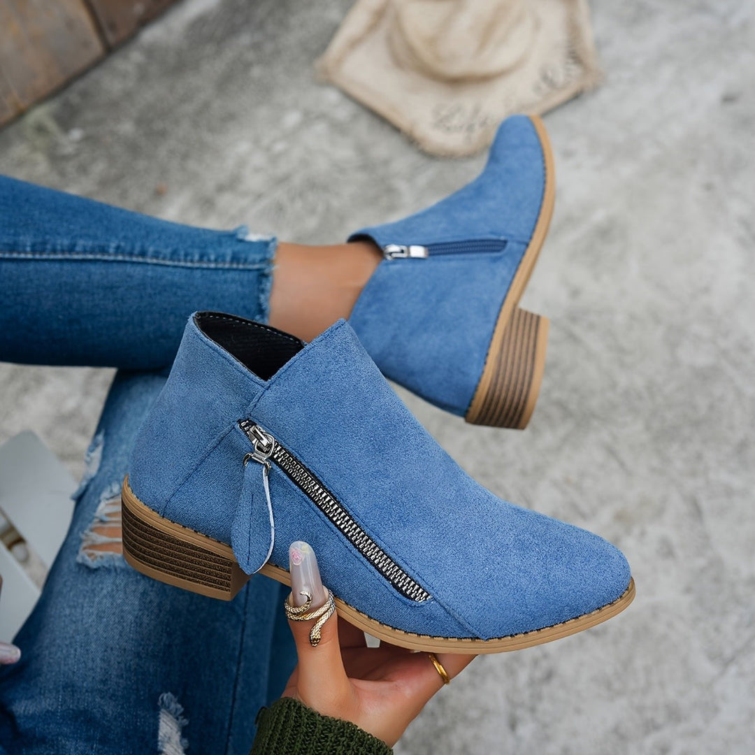 Denim blue suede ankle boots with side zip held in hand