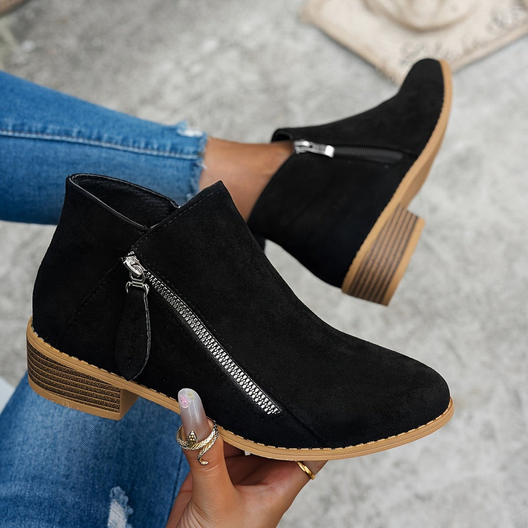 Black suede ankle boots with side zip fastening held in hand