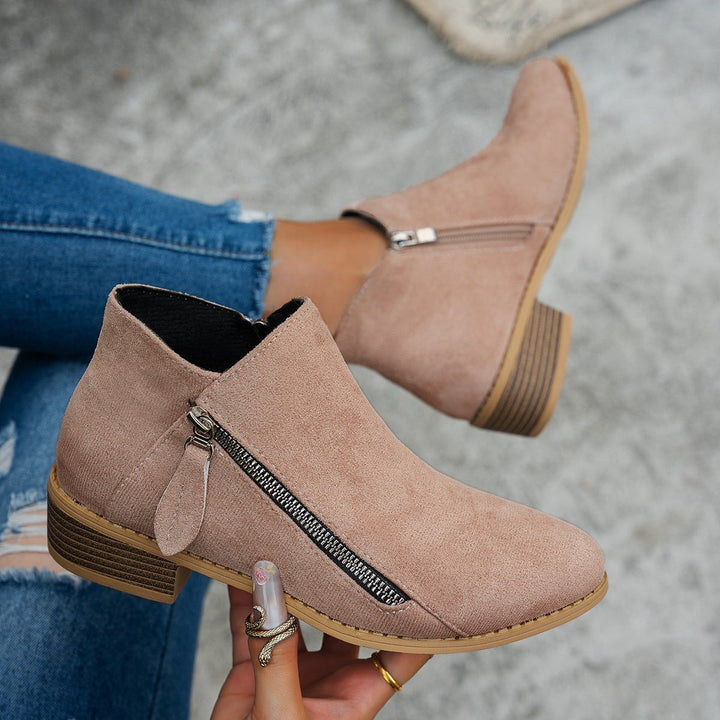 Dusky pink suede ankle boots with zip detail held in hand