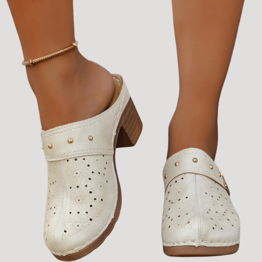Cream leather clog mules featuring perforated floral pattern and studded strap